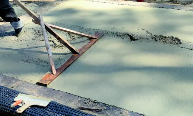Pracownik wyrównuje świeży beton, sprawdzając, jaka grubość chudziaka jest potrzebna. Narzędzie do zacierania betonu w akcji.
