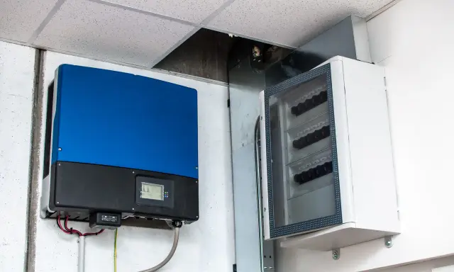 Niebieski falownik, kluczowy element instalacji fotowoltaicznej, zamontowany obok białej skrzynki z bezpiecznikami.