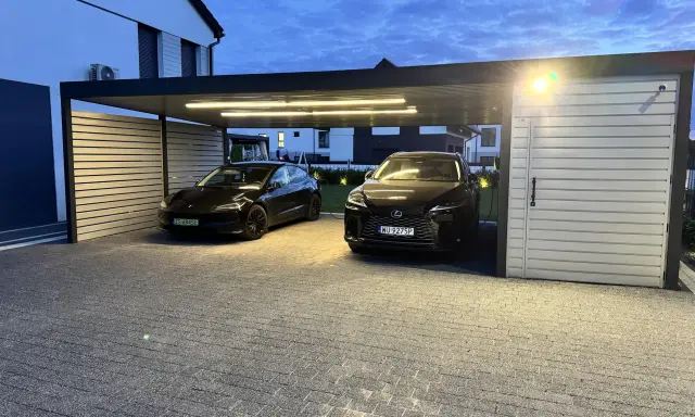 Nowoczesna wiata na 2 samochody projekt. Dwa czarne auta, Tesla i Lexus, stoją pod zadaszeniem z oświetleniem LED.