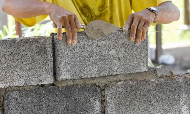 Murarz układa bloczek betonowy, dbając o jego wymiary i równość.