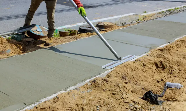 Pracownik wygładza świeży beton na chodniku. Jaki beton na wieniec? Ten budowlany jest idealny do takich prac.