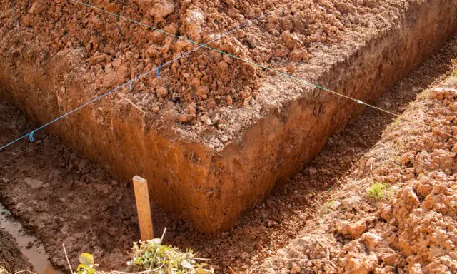Wyznaczone wykopy pod fundamenty, z widocznymi nićmi wyznaczającymi linie i drewnianym palikiem.