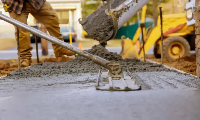 Pracownik wylewa beton, który będzie długo schnął w temperaturze 5 stopni. W tle koparka.