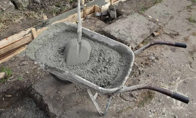 Taczka z betonem i łopatą czeka na wylanie zbrojenia ławy fundamentowej.