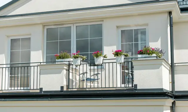 Białe okna pięknie komponują się z jasną, tynkowaną elewacją, tworząc elegancki wygląd. Balkon ozdobiony kwiatami dodaje uroku.