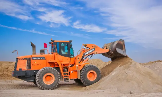 Pomarańczowa ładowarka Doosan DL300A zasypuje kopiec piasku, który może posłużyć jako żwir do betonu.