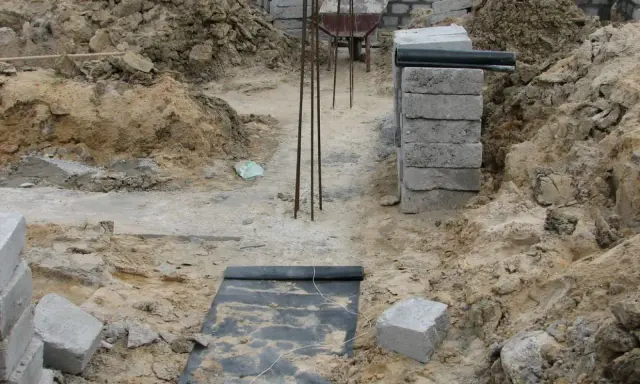 Budowa fundamentu z bloczków betonowych, zbrojenie i wózek widłowy w tle.