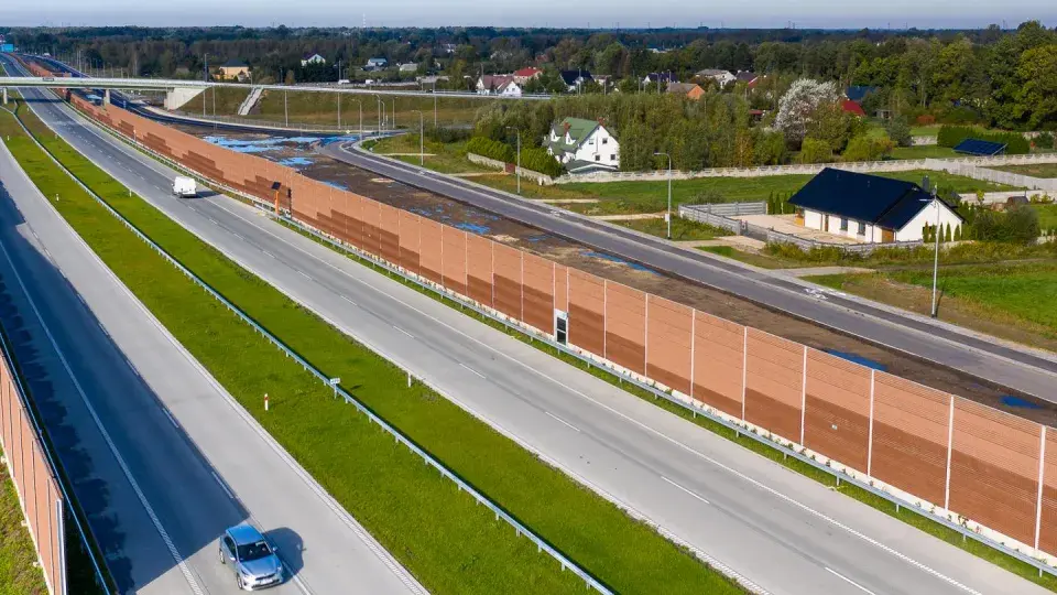Długa, brązowa ekran akustyczny od sąsiada chroni domy przed hałasem drogi szybkiego ruchu.