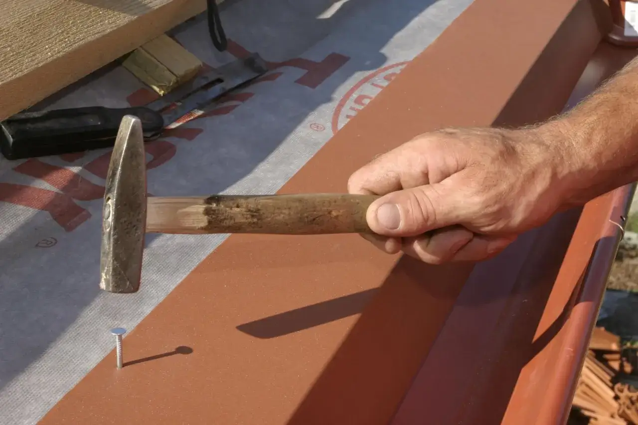 Dłoń z młotkiem przygotowuje montaż pasa nadrynnowego, wbijając gwóźdź.