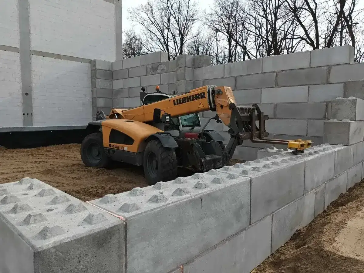 Żółty ładowacz Liebherr układa betonowe bloki, budując mur oporowy.