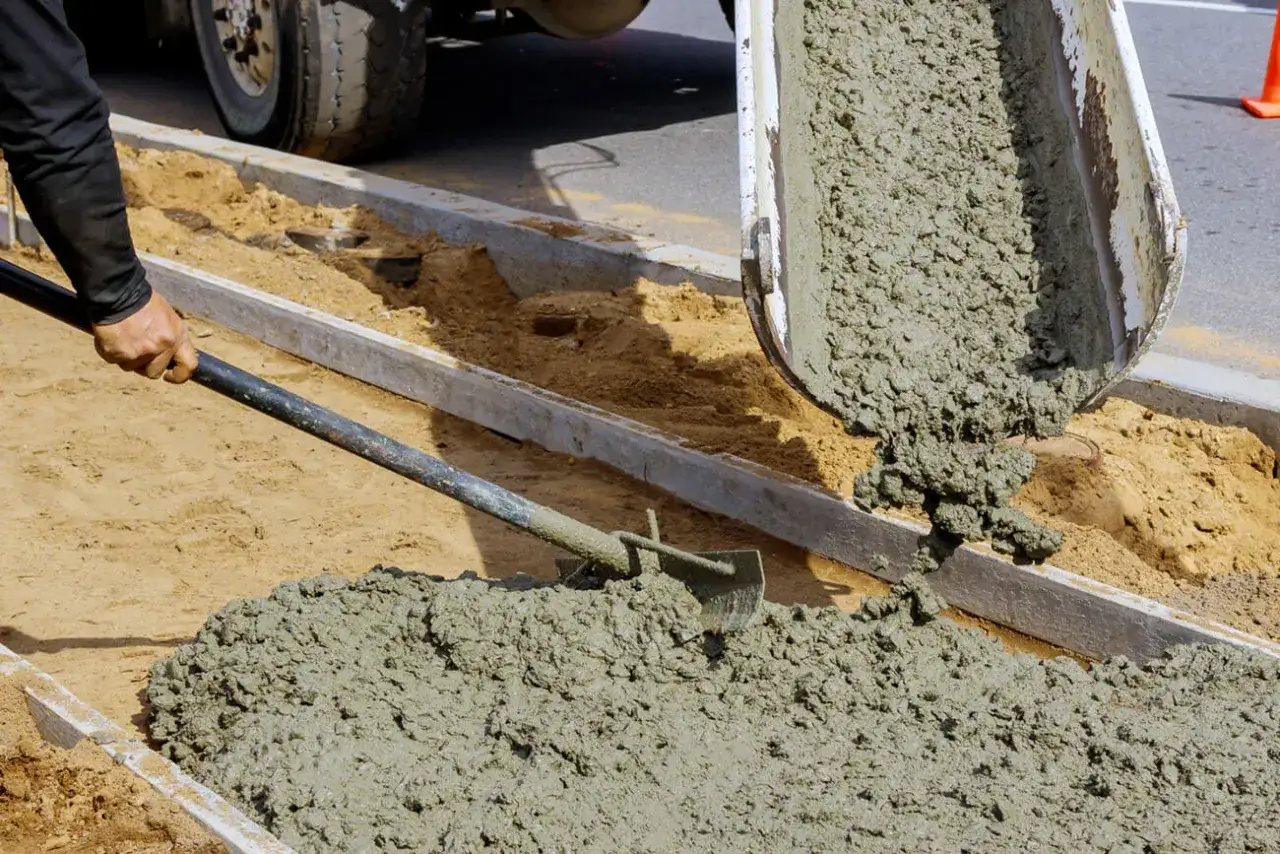 Robotnicy wylewają świeży beton, przygotowując teren pod budowę. To kluczowy etap, aby zrobić beton B25.