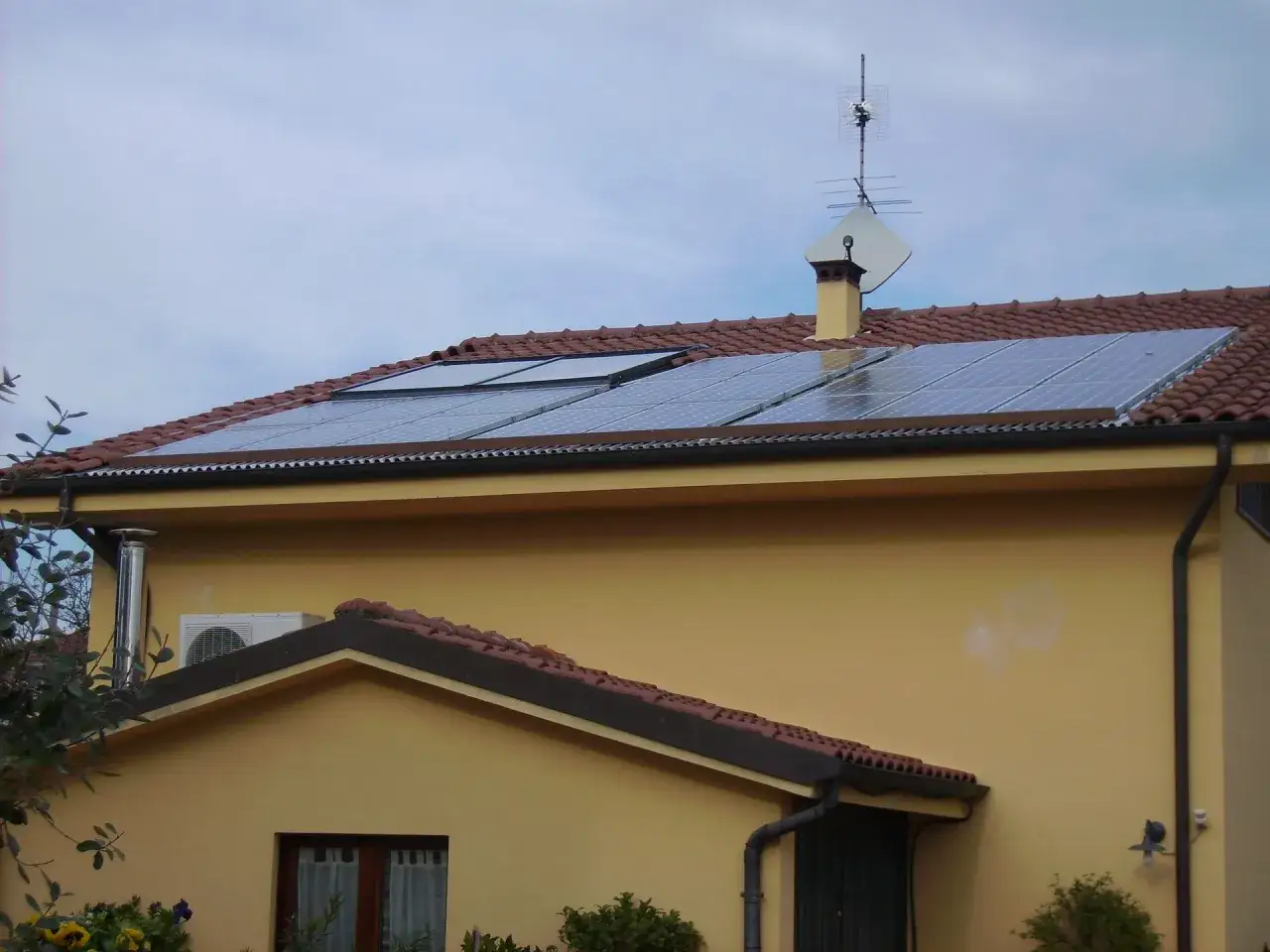 Instalacja PV na dachu żółtego domu. Panele słoneczne zbierają energię, pokazując, co to jest i jak działa.