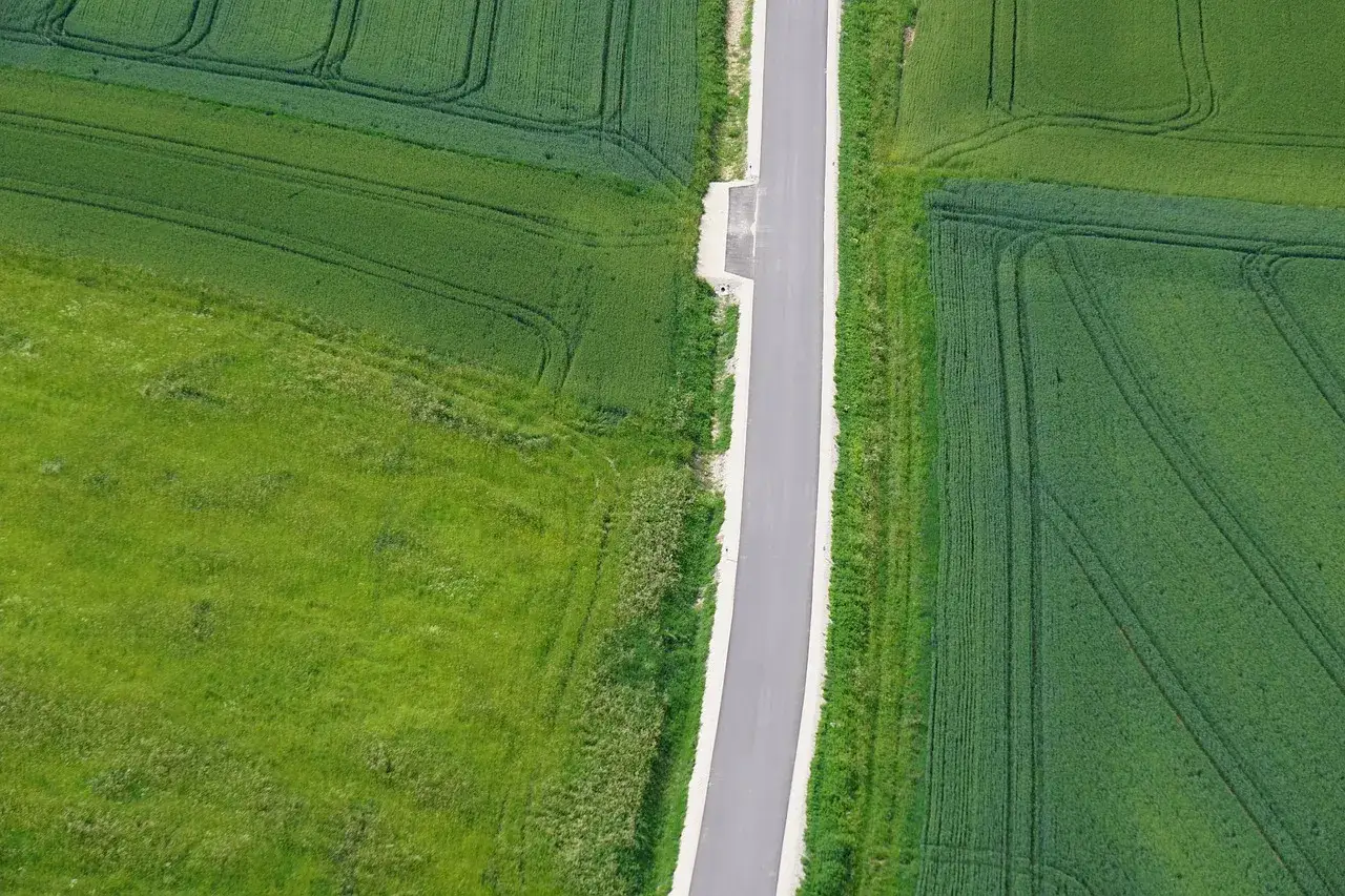 Wąska droga dojazdowa do działki prowadzi przez zielone pola zbóż i traw.
