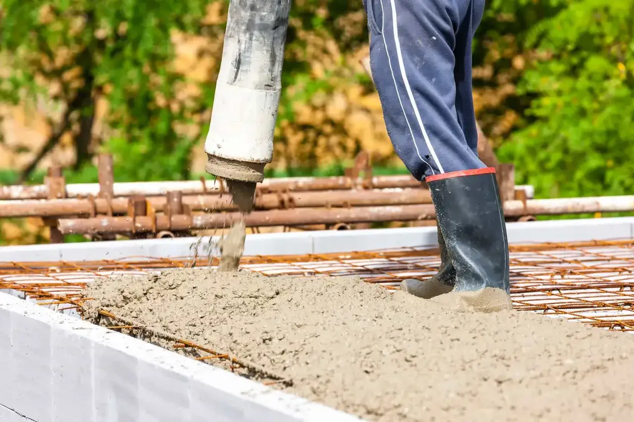 Betonowanie stropu. Pompa wylewa beton na zbrojenie. Pracownik w gumowcach stoi w świeżym betonie. Klasy betonu tabela.
