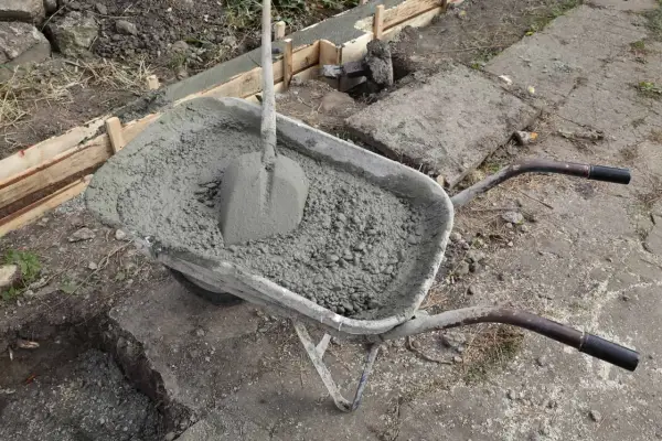 Taczka z betonem i łopatą czeka na wylanie zbrojenia ławy fundamentowej.